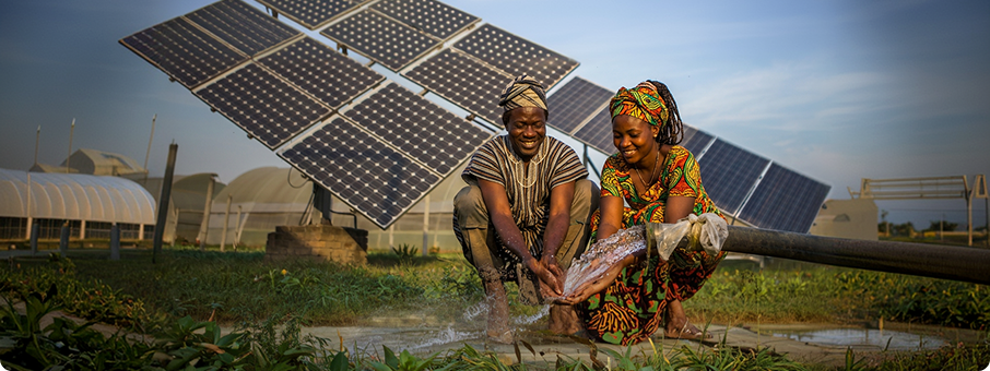 Workers in orange overalls carrying solar panels through a rural village in Africa