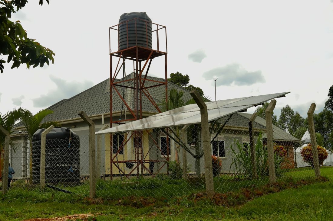 A water tank on a steel tower beside solar panels and a farmhouse